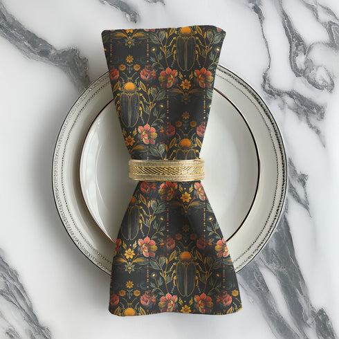 Set of four dark green cloth napkins with a repeating pattern of golden beetles, coral flowers, and ochre wildflowers in an intricate botanical and entomological design.